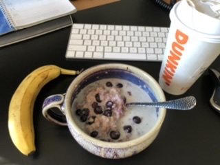 Bowl of steel-cut oatmeal with blueberries, a banana, and a Dunkin’ Coffee for breakfast