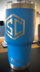 Flip side of 24-ounce blue and silver hot/cold Yeti mug with "SC" for "SteadyCare" on it.